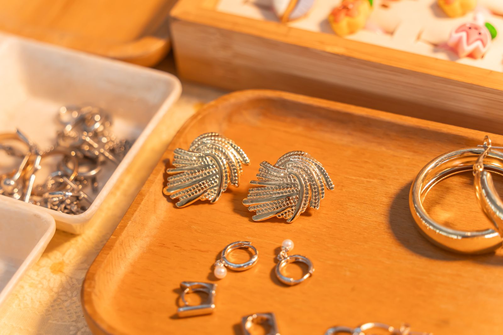 Gold leaf earrings, small silver hoops and a ring on an orange wooden tray