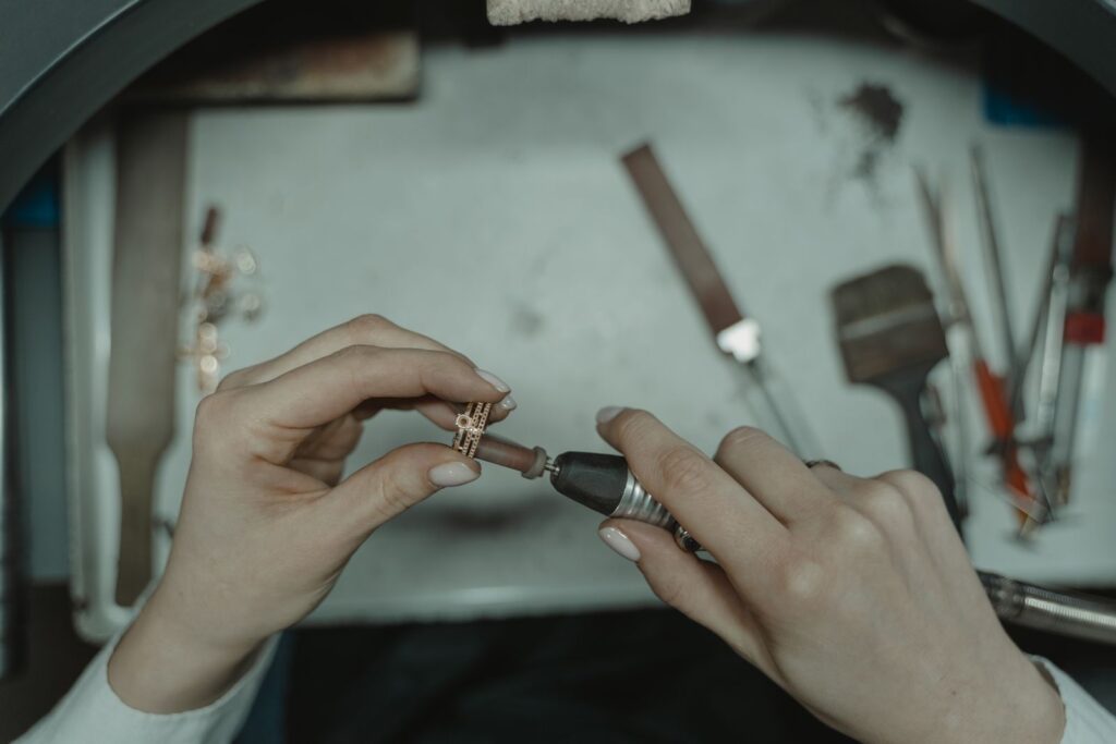 Hands polishing a rose-gold ring with a rotary tool over the bench tray