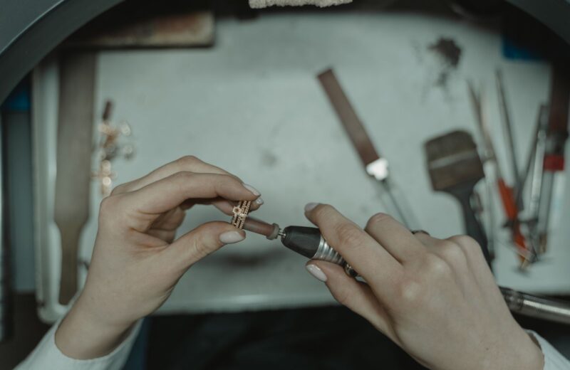 Hands polishing a rose-gold ring with a rotary tool over the bench tray