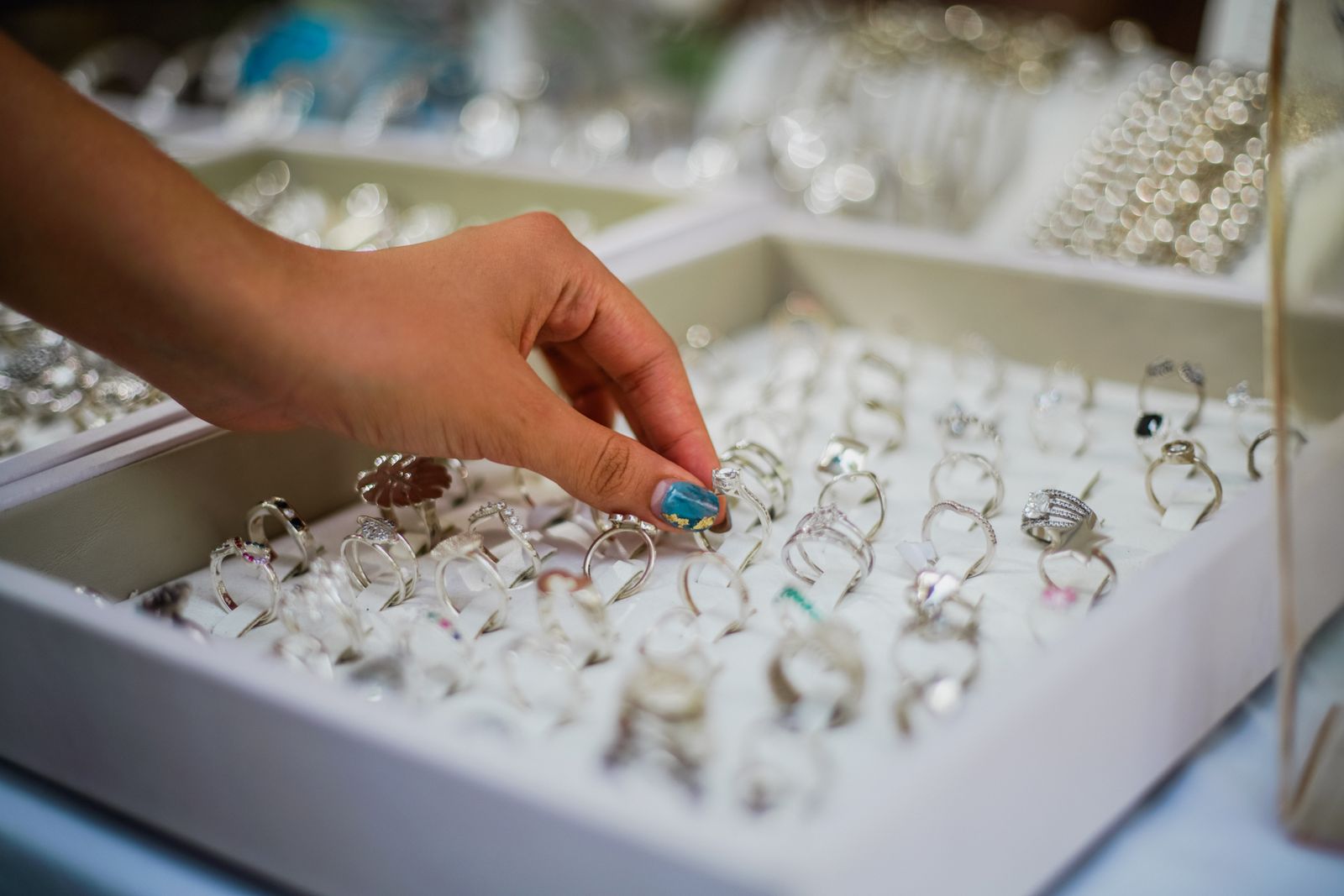 A hand picking a silver ring from a white display tray full of rings