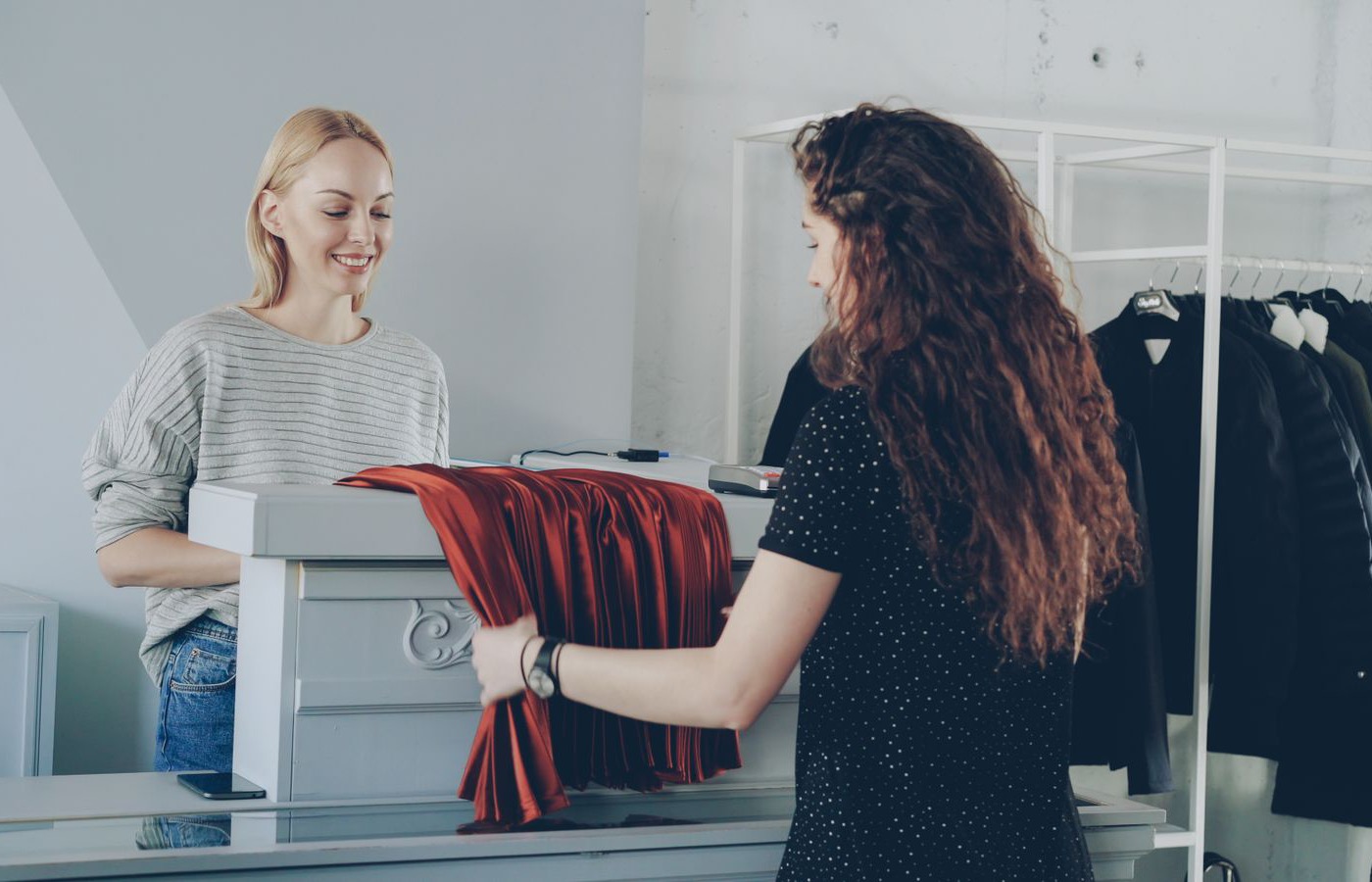 A customer handing a pleated rust skirt across the shop counter to the woman behind it