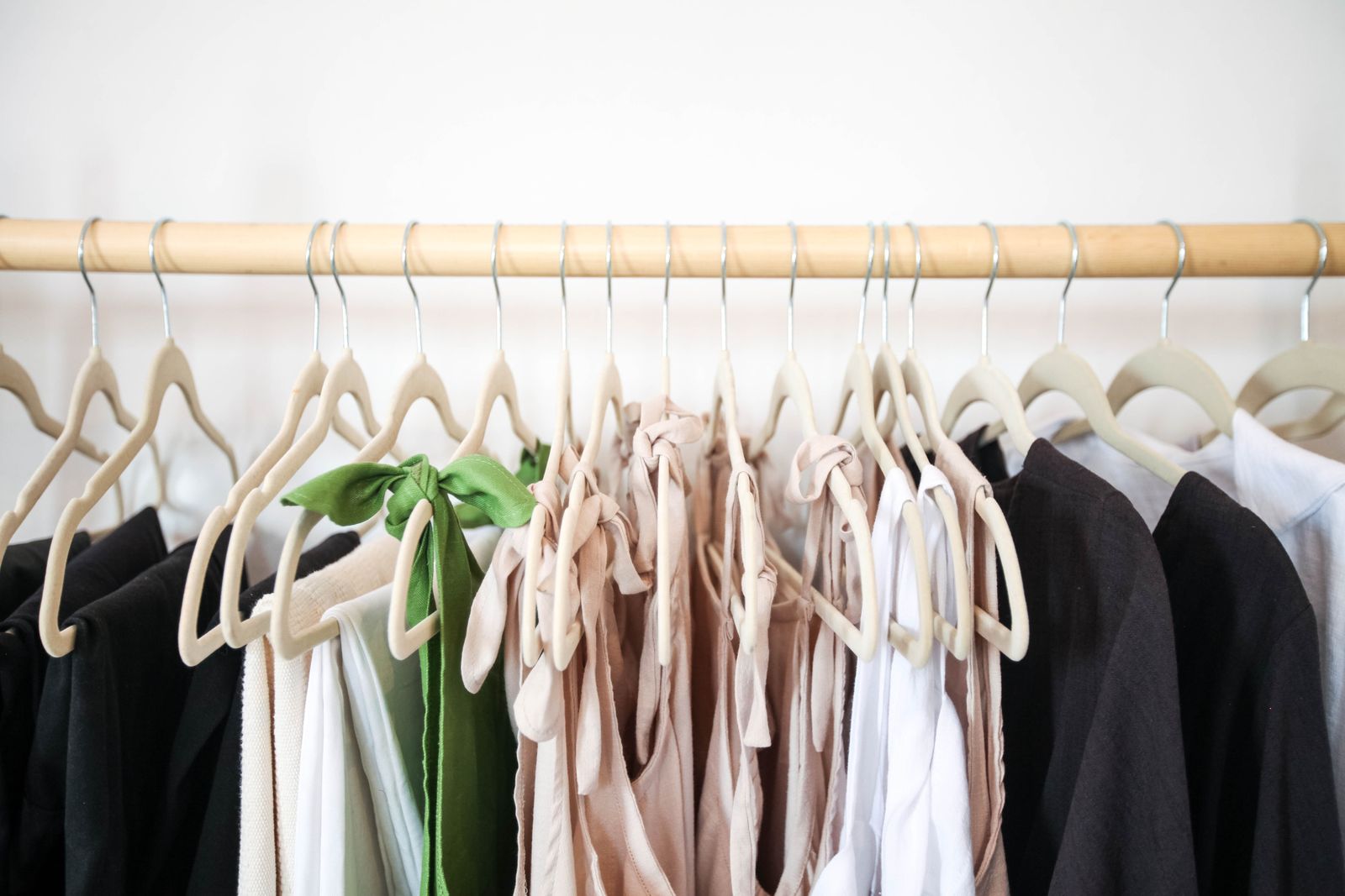 Linen tops and dresses in black, white, blush and green on felt hangers along a wooden rail