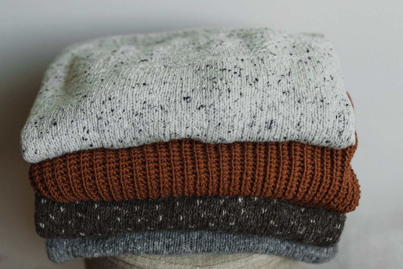 A stack of folded jumpers in grey, rust and charcoal