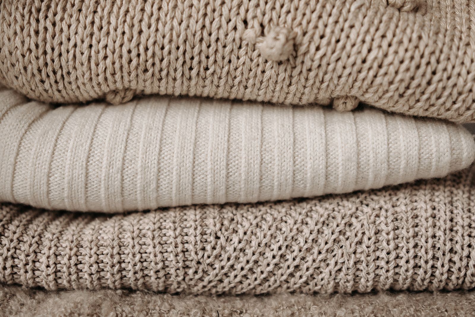 A close-up of folded knitwear in oatmeal and cream, stacked on a table