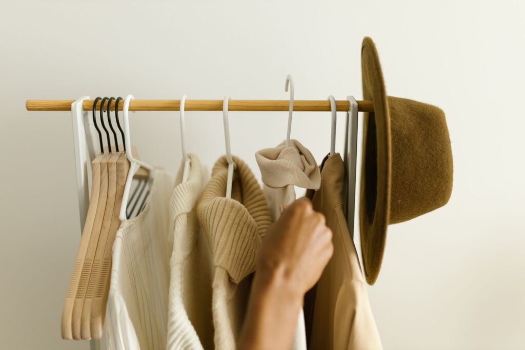 A hand choosing between cream and camel pieces on a small rail, with a felt hat on the end
