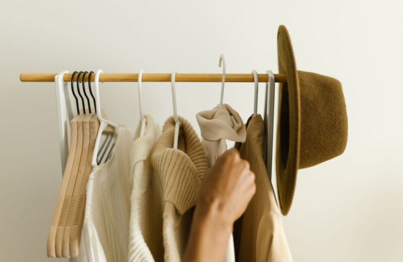 A hand choosing between cream and camel pieces on a small rail, with a felt hat on the end