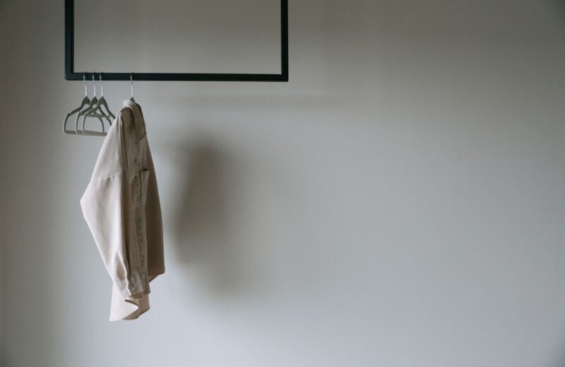 A single beige jacket on a slim metal rail against a white wall