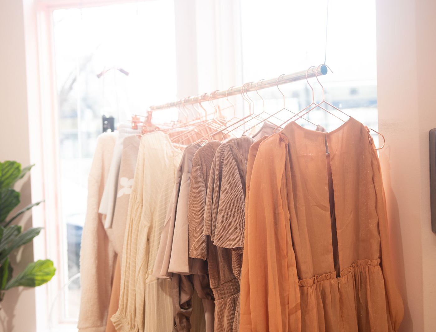 A rail of dresses in pale apricot, sand and cream on copper hangers by a bright shop window