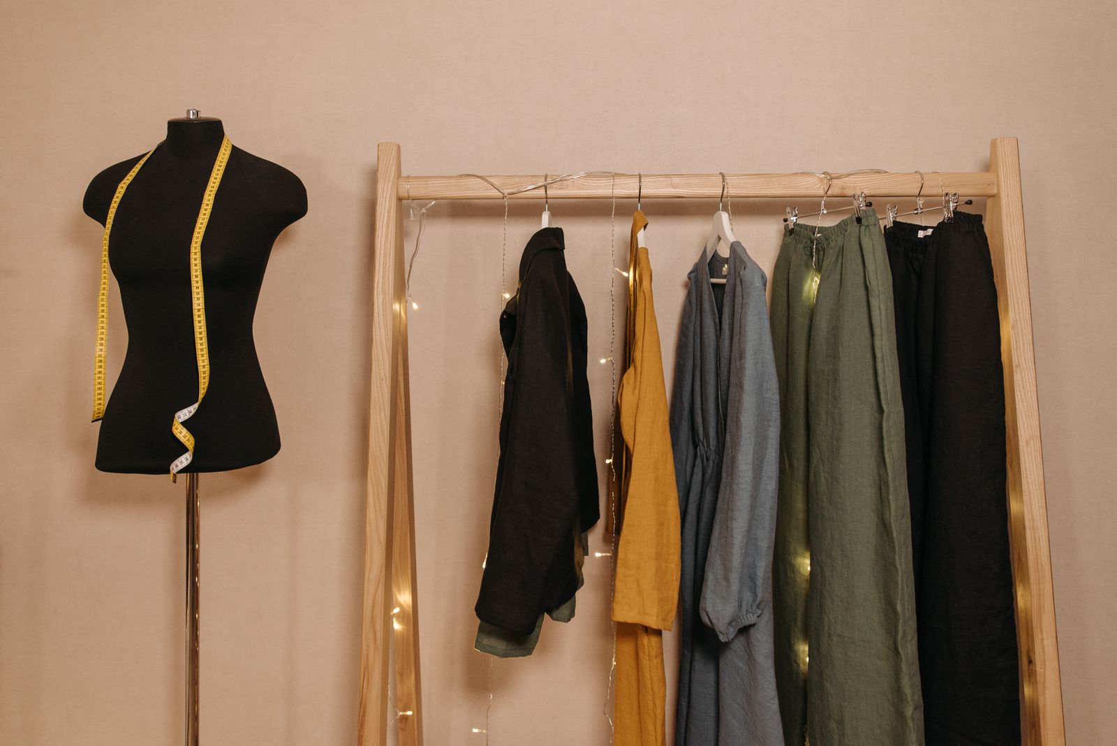 A wooden rail of linen jackets, a dress and trousers next to a dress form with a tape measure