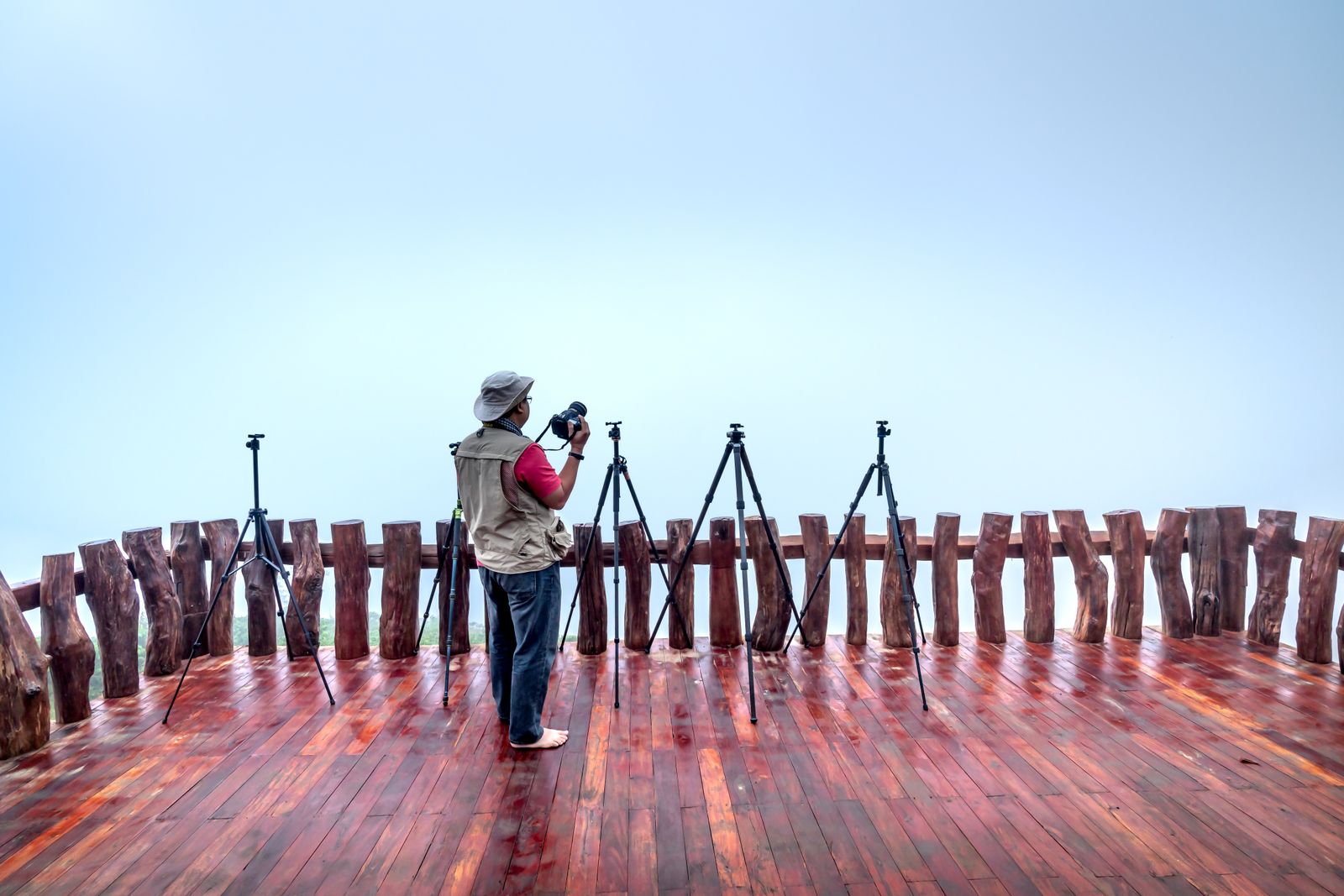 A photographer setting up tripods on a long wooden terrace, seen from far away against a white sky