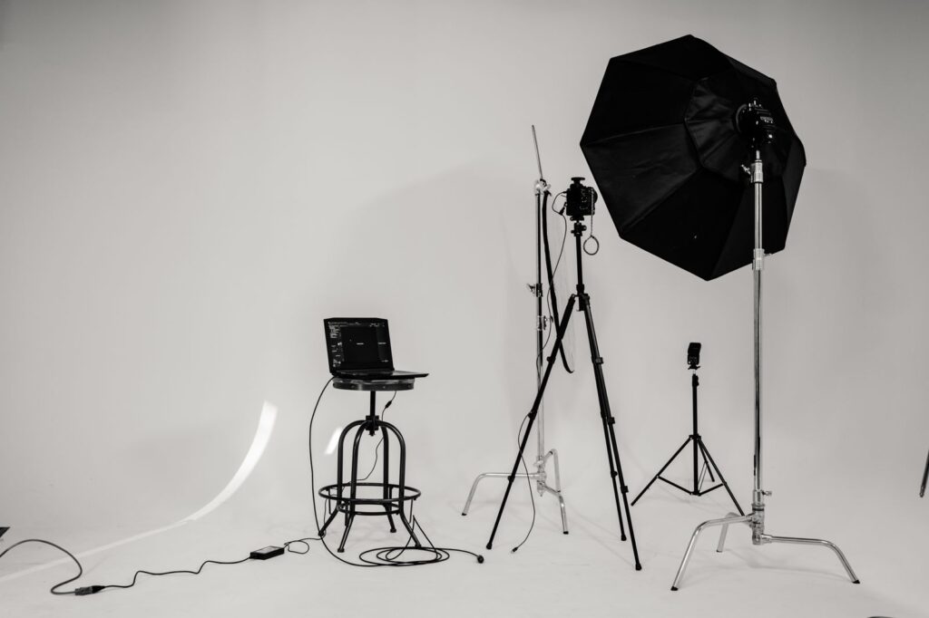 An empty photo studio with lights on stands and a white backdrop, in black and white