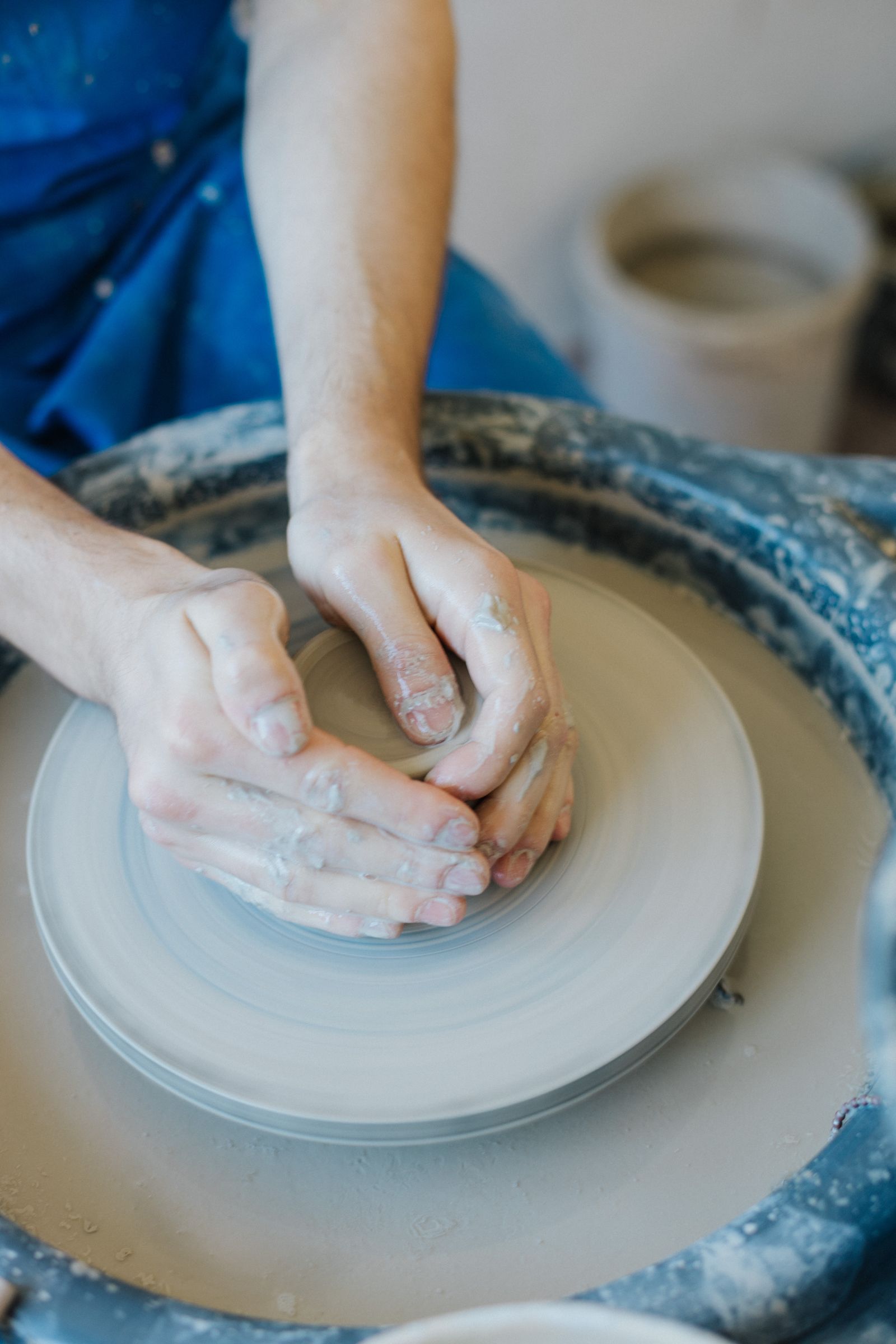 Hands shaping wet clay on a potter's wheel, seen from above