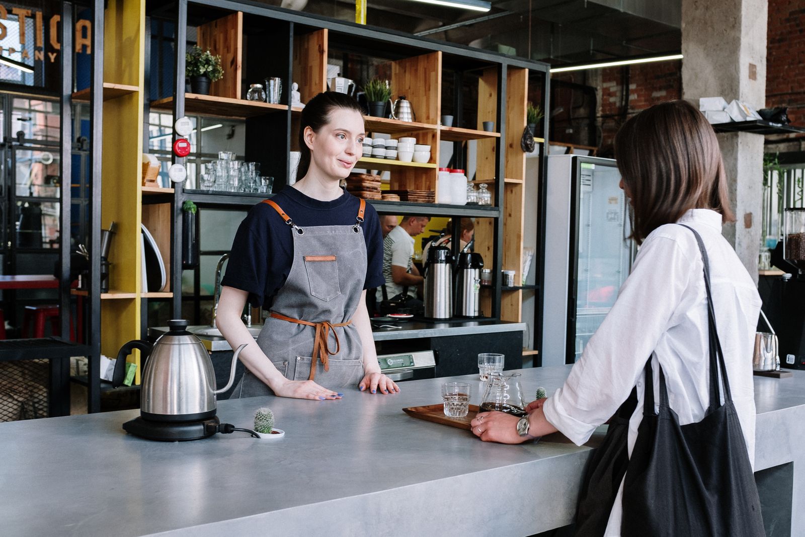 A barista in an apron serving a customer across a steel café counter