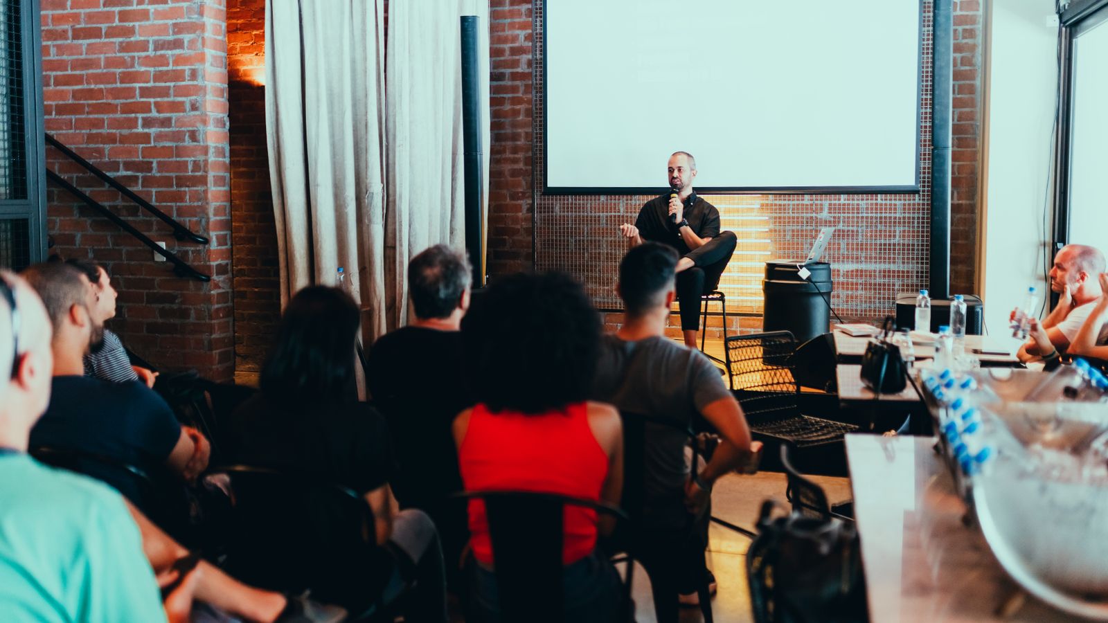 People listening to a speaker at a meeting in a brick-walled room