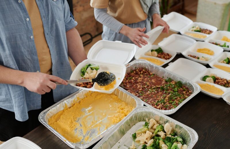 Hands filling takeaway trays with rice, vegetables and salad