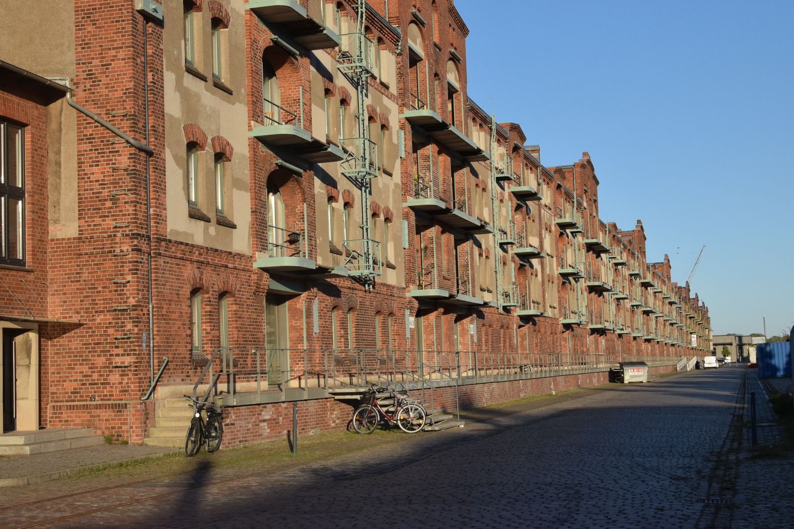 A long brick warehouse in sunlight with bicycles parked outside