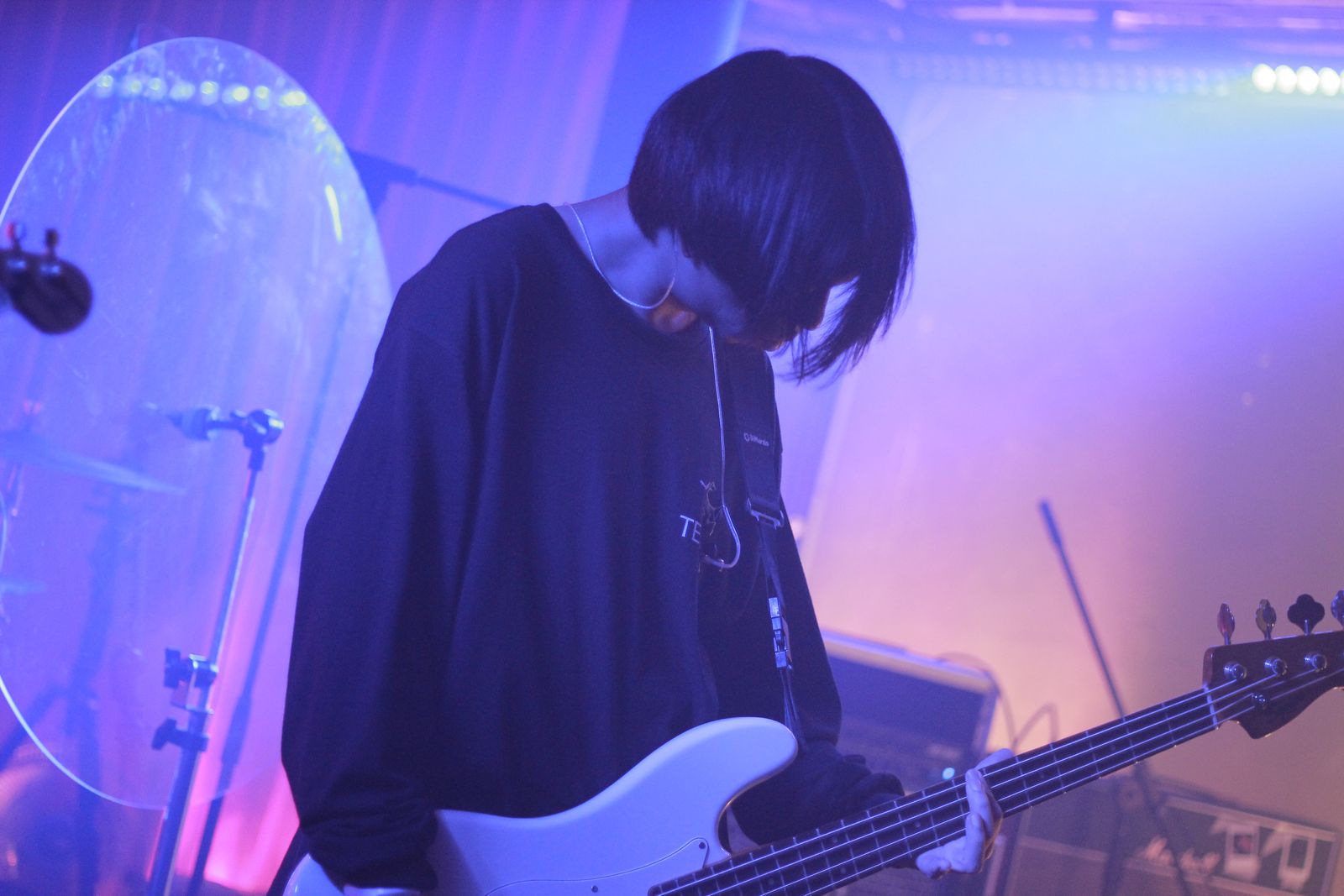 A bass player on stage in violet light, head down over the strings