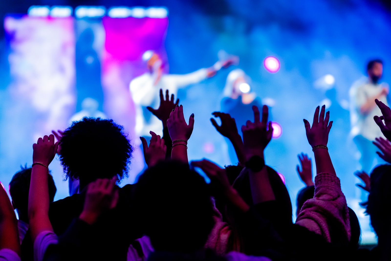 Hands raised in a crowd in front of a lit stage