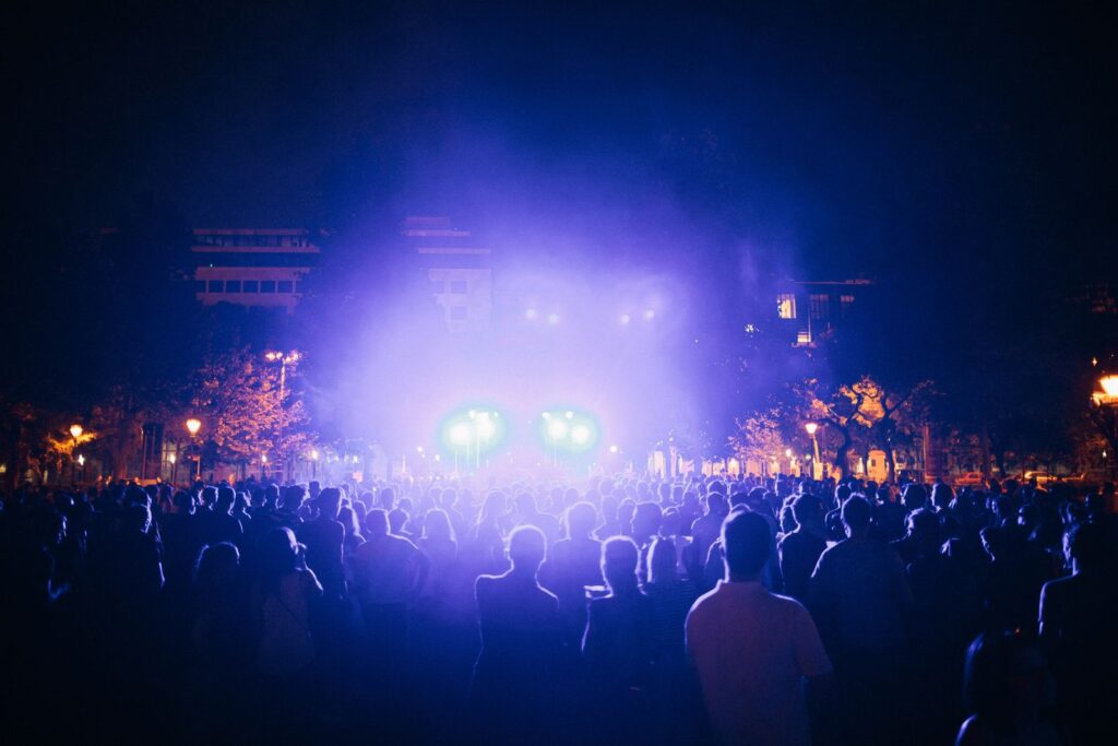 An outdoor festival crowd at night in front of a stage lit in violet