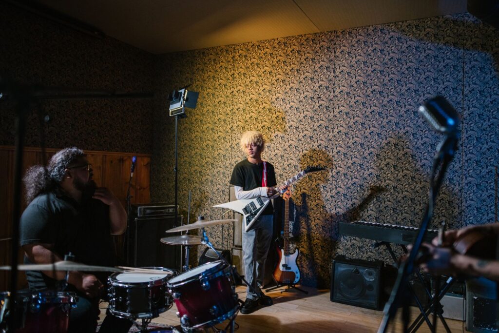 Band members playing guitar, bass and drums in a small rehearsal room