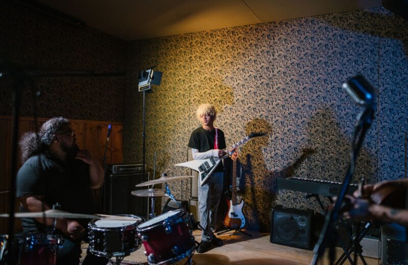 Band members playing guitar, bass and drums in a small rehearsal room