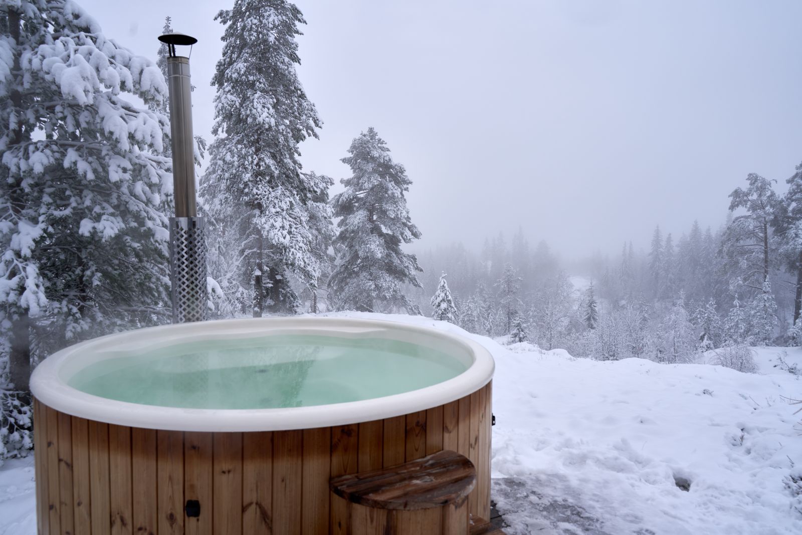 A round wooden tub of water outdoors among snowy fir trees