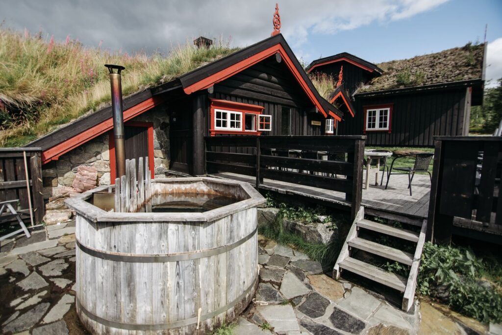 A wooden tub on a stone terrace in front of a turf-roofed timber cabin