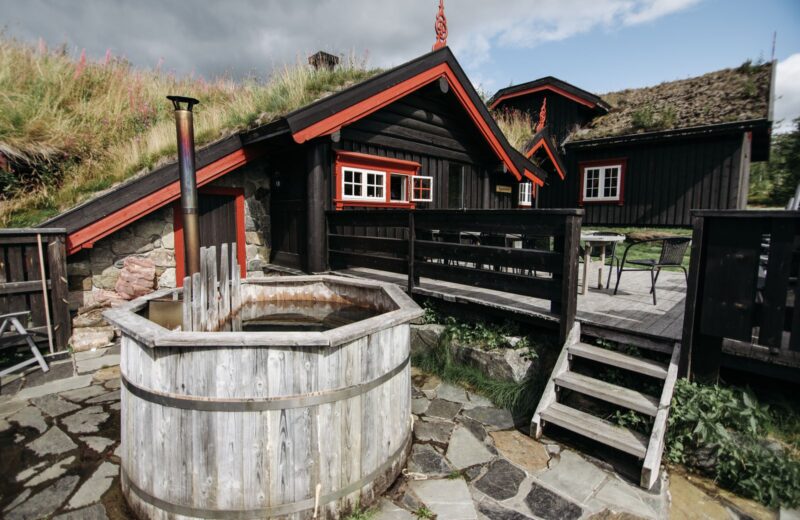 A wooden tub on a stone terrace in front of a turf-roofed timber cabin