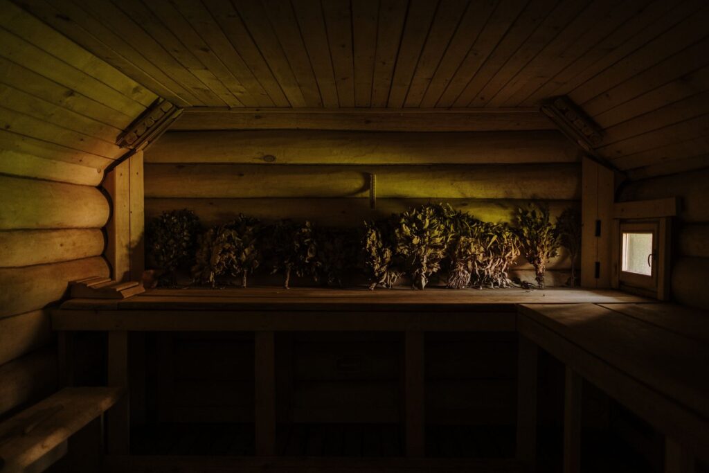 A dim log sauna with bunches of dried leaves hanging over the benches