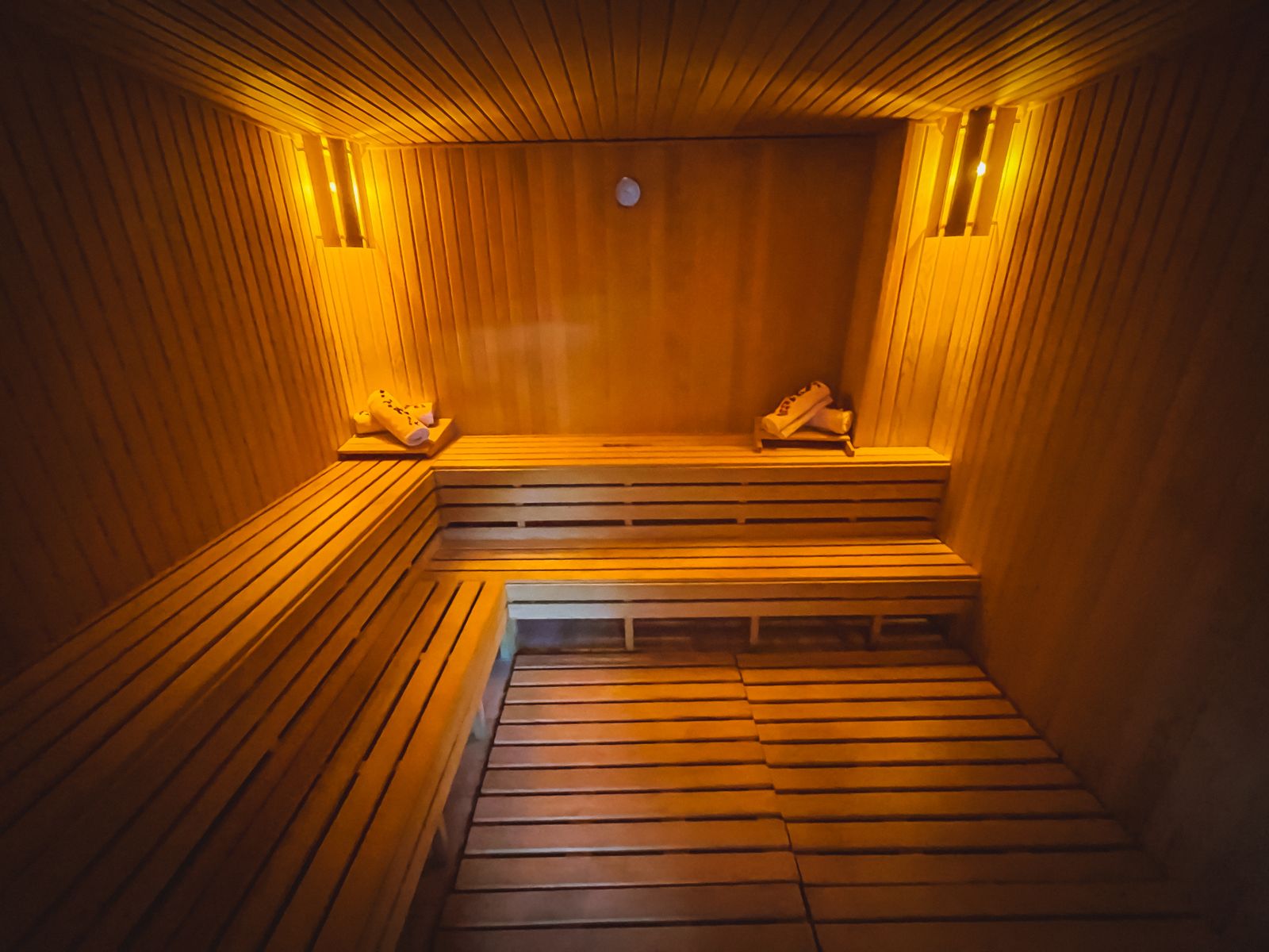 Inside a wooden sauna: two rows of benches along the walls under warm wall lights