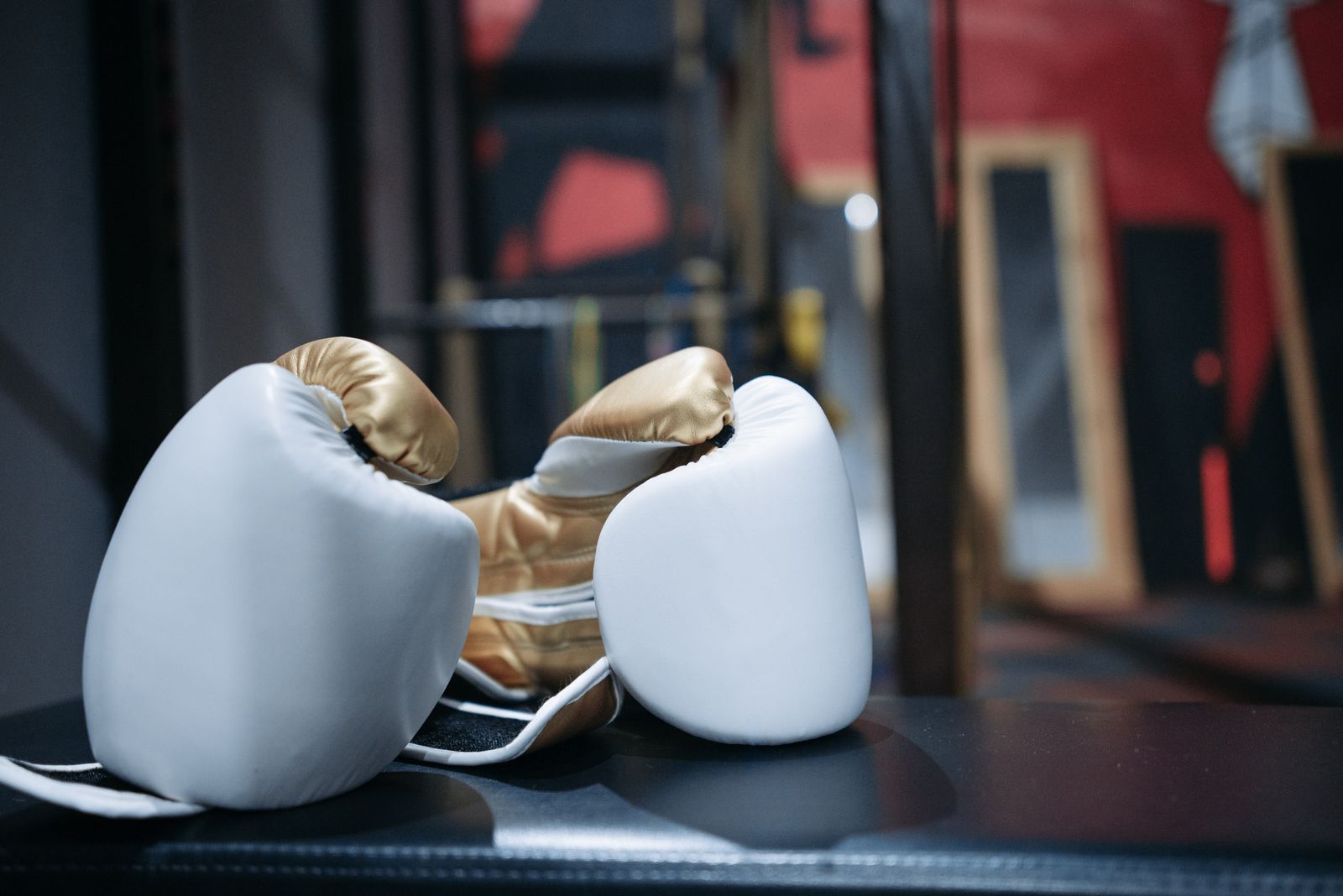 A pair of white and gold boxing gloves on a dark bench in a gym