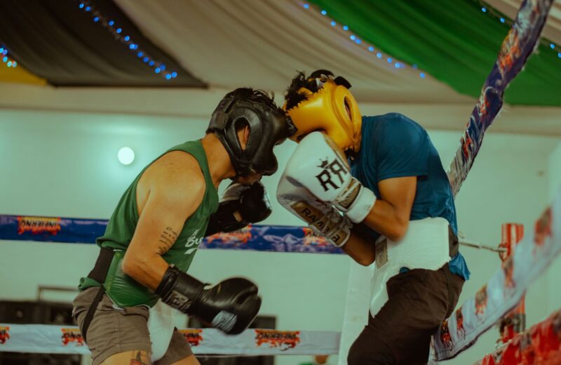 Two boxers in headgear and gloves trading punches at close range in a training ring
