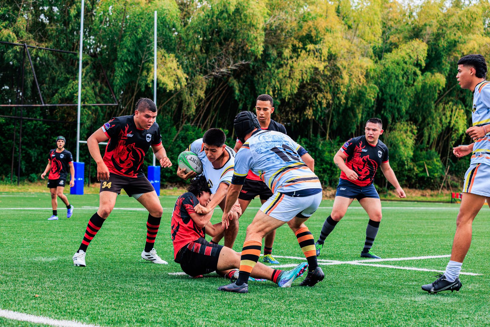 Rugby players in red and white shirts contesting the ball at a ruck on a green pitch
