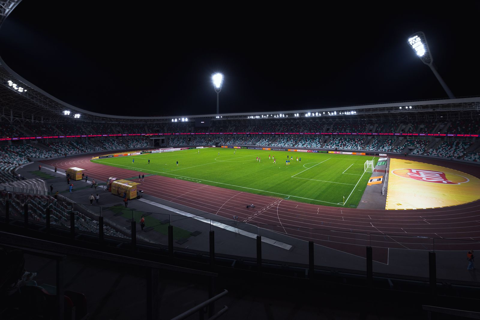 An empty stadium at night, the pitch lit bright green under the floodlights