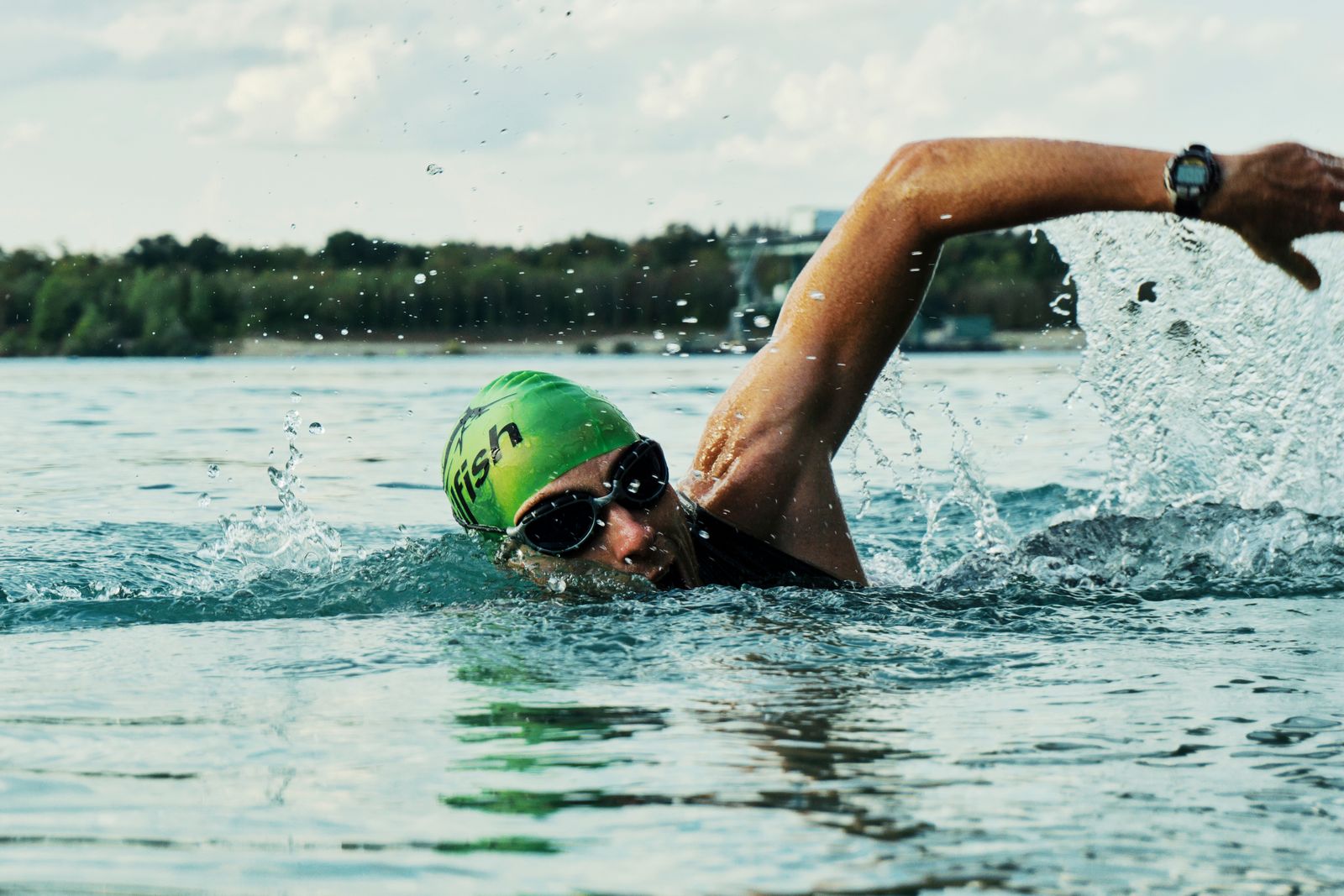 A swimmer in a green cap and goggles doing front crawl in open water on a bright day