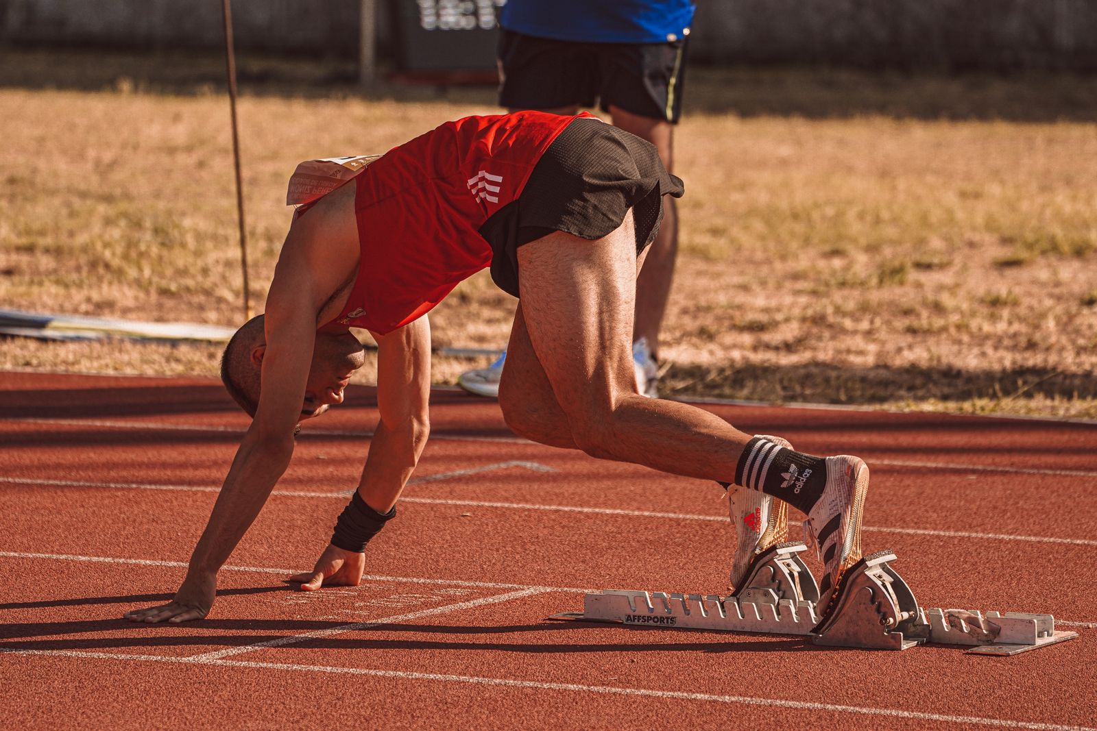 An athlete in red pushing off from the starting blocks on an outdoor track