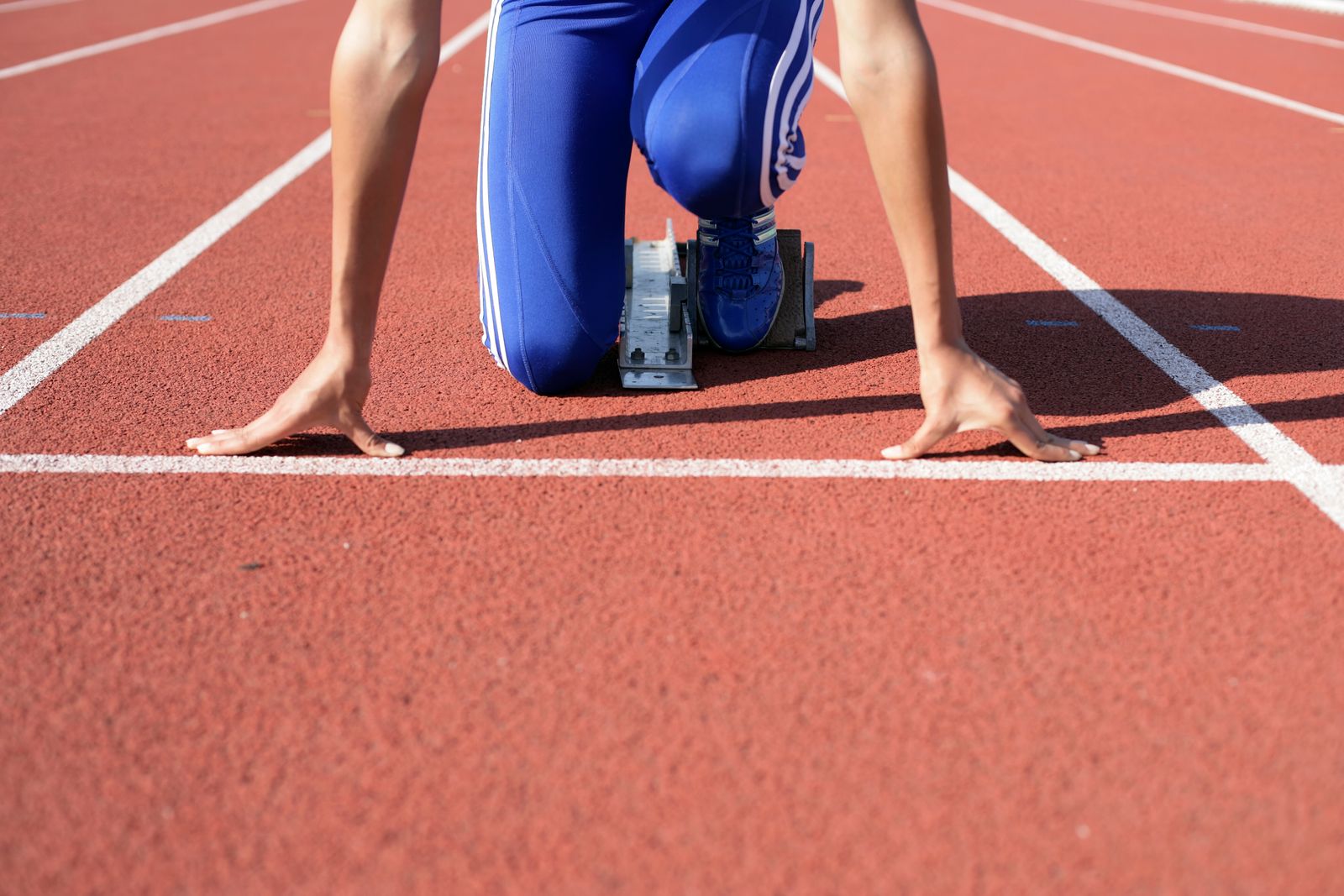 A sprinter's hands on the white line of a red running track, crouched in the starting blocks
