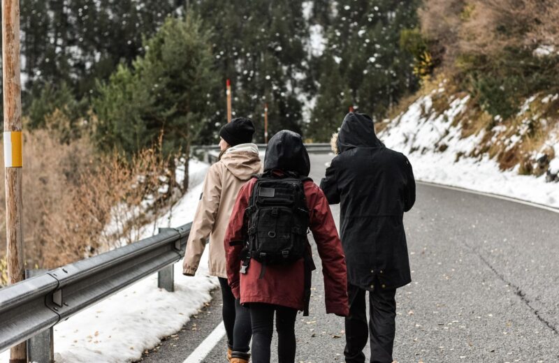 Three walkers in hooded winter jackets and a backpack on a mountain road, snow on the verges