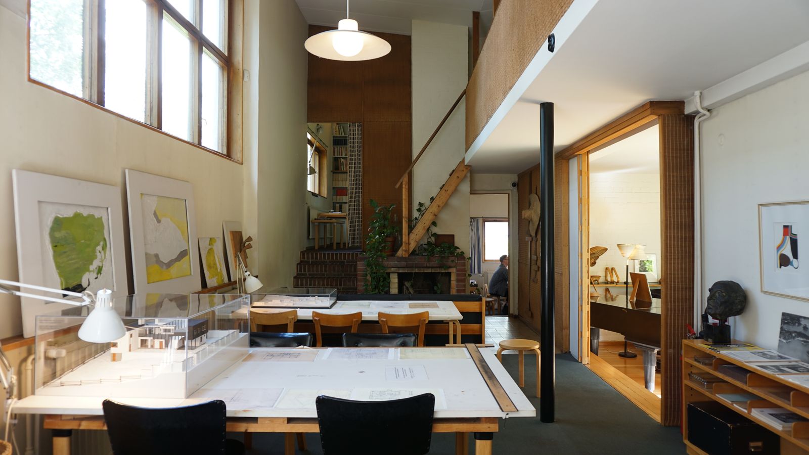 A bright studio with long shared tables, shelves and tall windows