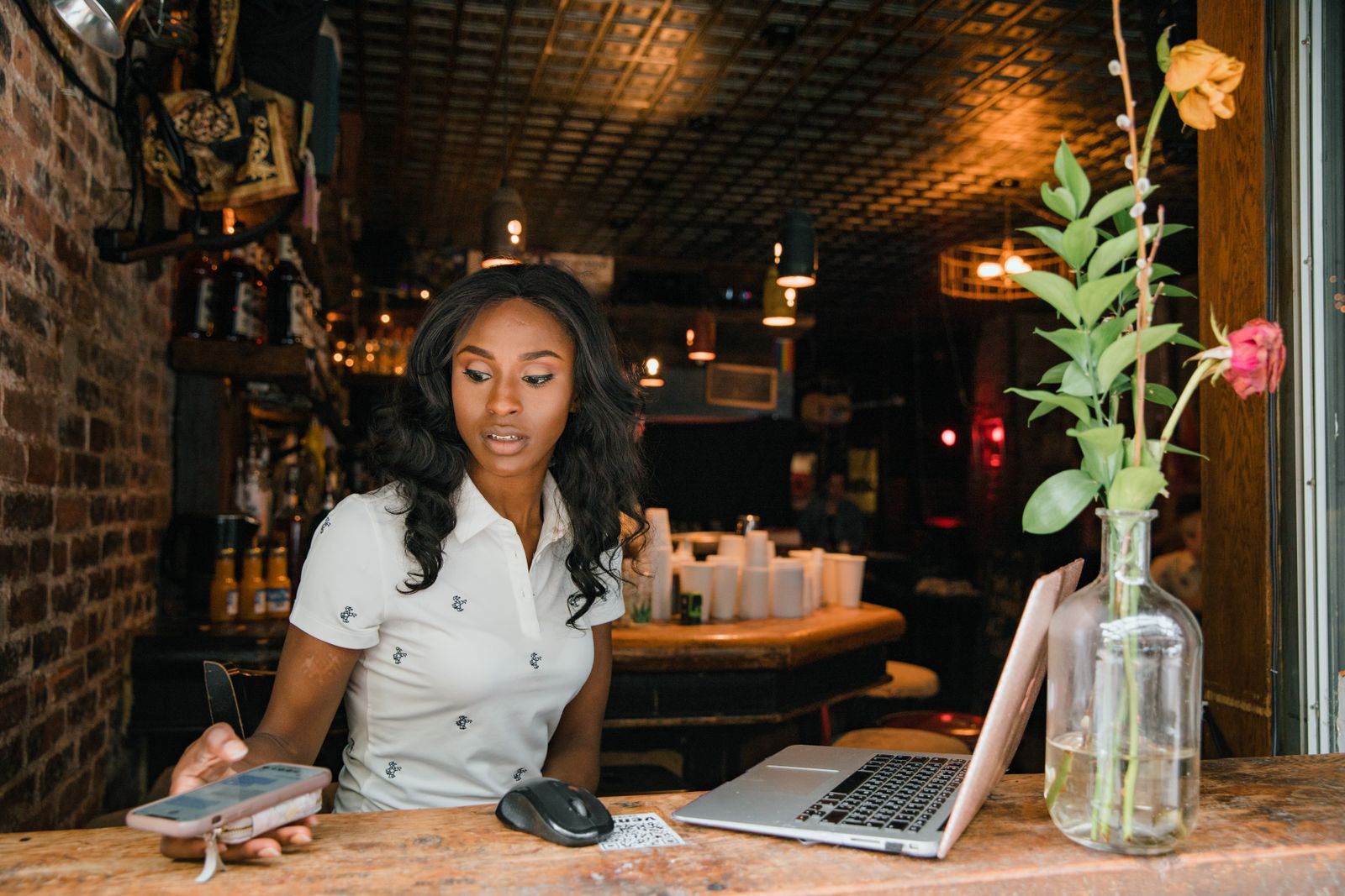 A cafe owner at the counter checking her phone with a laptop open beside her