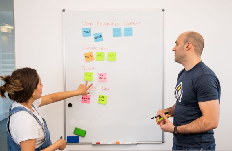 Two colleagues planning with coloured sticky notes on a whiteboard