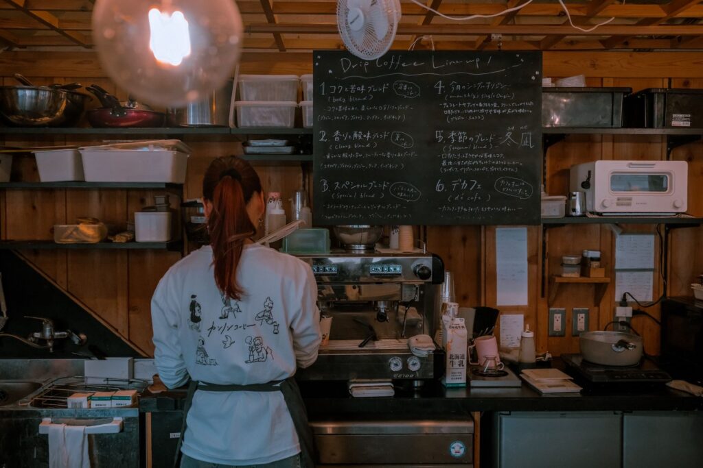 A barista working behind a cafe counter under a chalkboard menu
