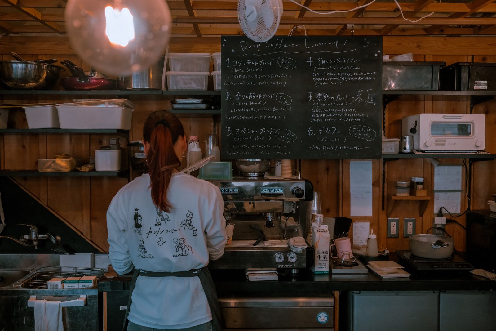 A barista working behind a cafe counter under a chalkboard menu