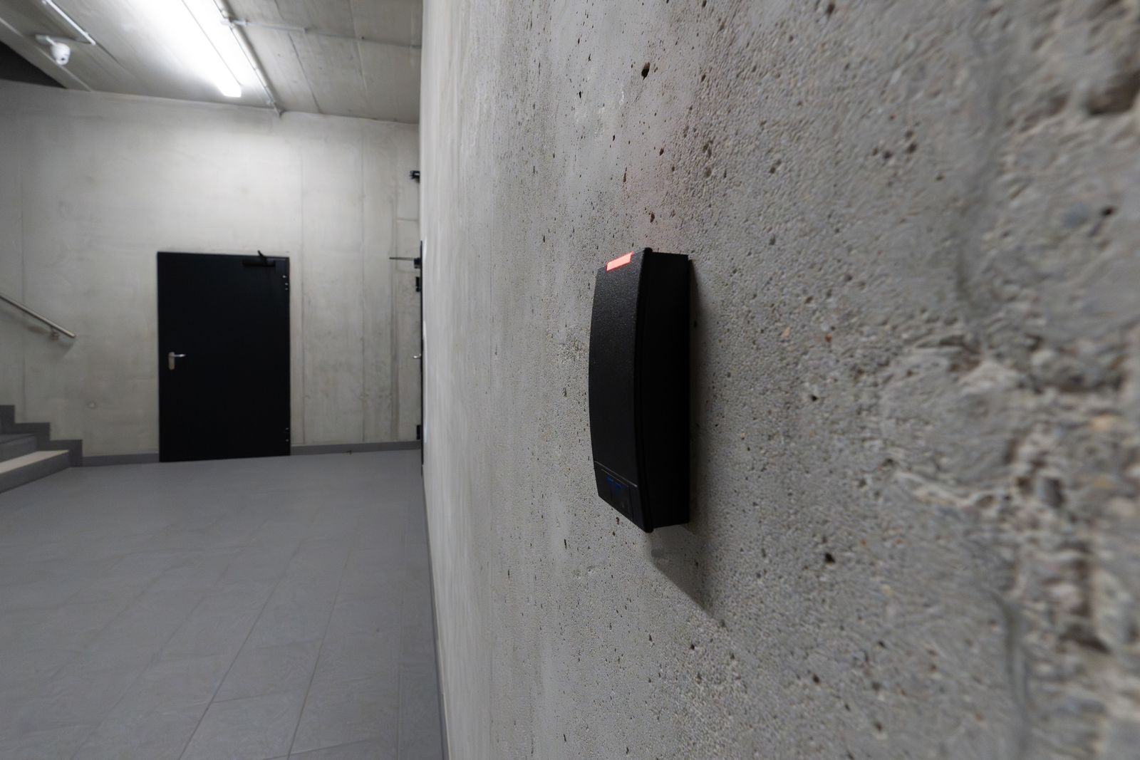 A card reader on a concrete wall in a corridor leading to a steel door
