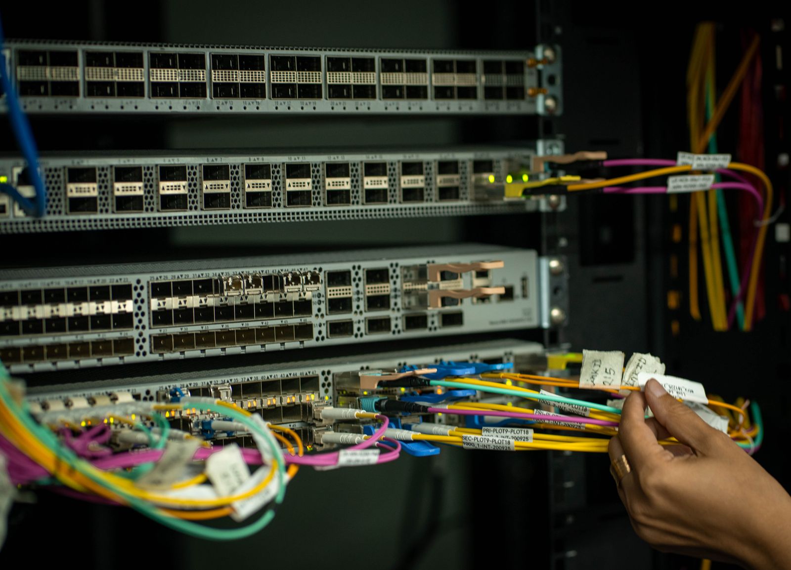 A hand sorting fibre optic patch cables in a server rack