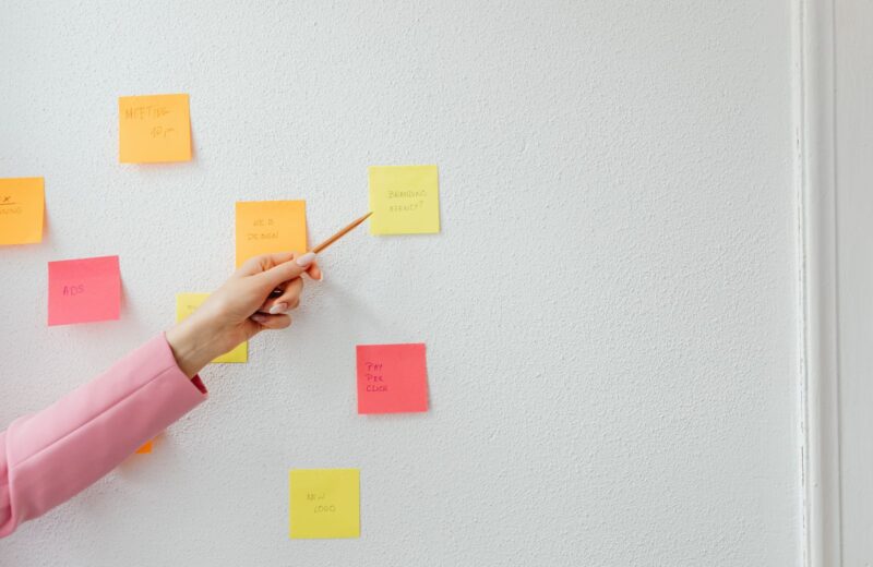 A hand arranging coloured sticky notes on a white wall