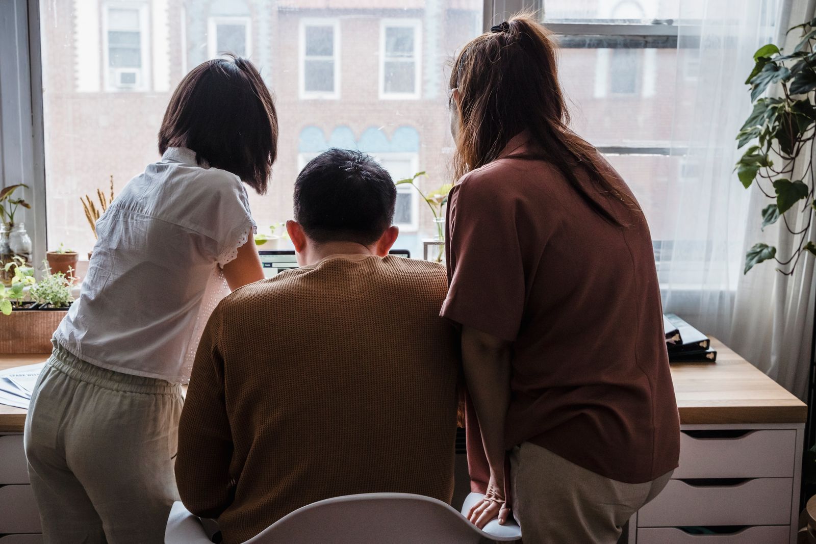 Three colleagues looking at a laptop together by a large window