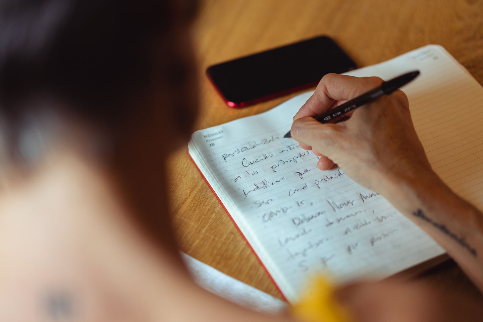 A person writing a handwritten list in a notebook at a wooden table