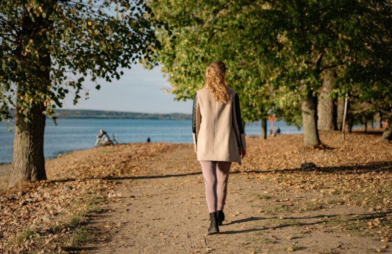 A woman walking away along a tree-lined lakeside path in autumn