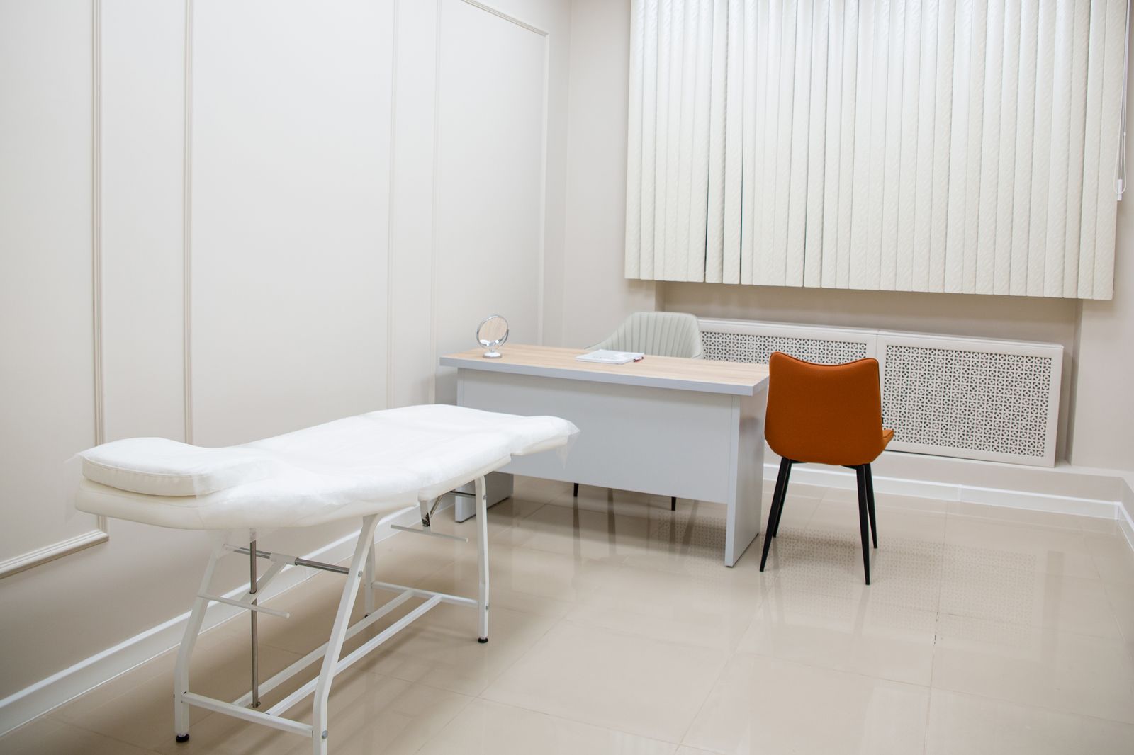 An empty, bright consulting room with a desk, two chairs and an examination couch